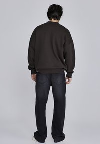 Ciemnobrązowy, oversize'owy sweatshirt w połączeniu z ciemnoniebieskimi dżinsami. Sweatshirt ma okrągły dekolt i ściągacze przy rękawach; dżinsy mają dwie tylne kieszenie.