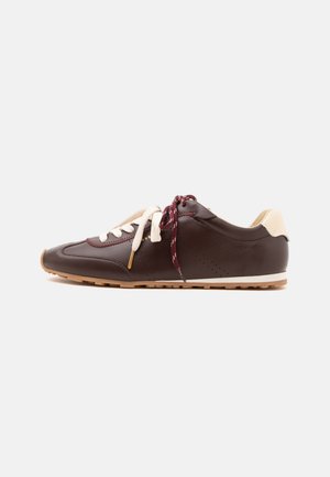 Baskets en cuir marron foncé avec talon beige, lacets bicolores blancs et bordeaux, semelle marron clair sur fond blanc.