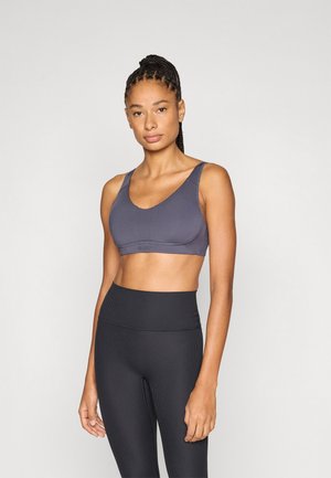 Športni modrček v temno sivi barvi z širokimi naramnicami, okroglim izrezom in brezšivno zasnovo. Kombiniran z visokim pasom črnih rebrastih pajkic.