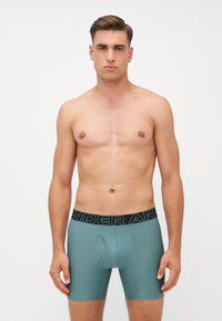 Pánske teal boxerky s čiernym pásom a logom "UNDER ARMOUR". Hladká textúra a priliehavý strih s tvarovaným vreckom.