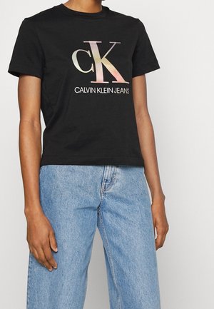 Černé bavlněné tričko s velkým vícebarevným gradientním logem "CK" a textem "CALVIN KLEIN JEANS" níže, s krátkými rukávy a volnějším střihem.