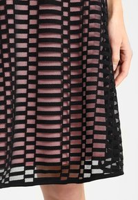 Svart nätkjol med horisontellt och vertikalt randmönster. Har en lagerdesign med ett rosa underlager, strukturerad tyg och fållfinish.