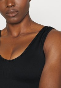 Top de tanque preto com nervuras, decote em V profundo e alças largas, apresentando uma textura suave e um design ajustado, acentuando os ombros.