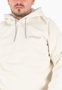 Beige hoodie met geribbelde manchetten en zoom, voorzien van een blauwe gevlochten trekkoord en een klein, reliëf logo op de borst. Zachte stoftextuur.
