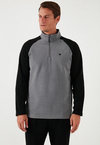 Grå fleece-pullover med sorte raglanærmer, kvart-zipkrave og lille logo. Blød tekstur, afslappet pasform og slankt design.