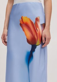 Een blauwe rok met een grote, levendige oranje tulpafbeelding. Het materiaal lijkt glad met een vloeiende vorm en een zachte textuur.