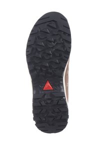 Suela de zapato de goma negra con surcos profundos, que presenta una superficie texturizada y un acento triangular rojo. Parte superior de color marrón claro visible en el borde.