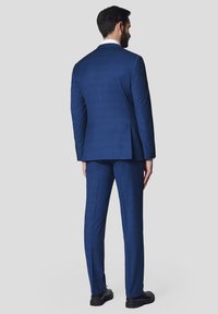Granatowy garnitur z teksturowanym wykończeniem, z pojedynczym rozcięciem z tyłu i spodniami z płaskim przodem, w połączeniu z czarnymi butami.