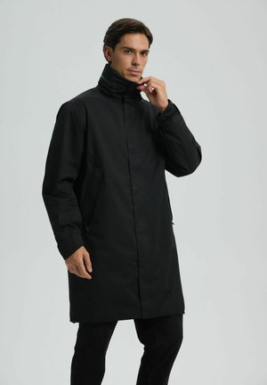 Schwarzer wasserdichter Mantel mit hohem Kragen, vorderem Knopfverschluss, seitlichen Taschen und langen Ärmeln, entworfen mit einer geraden Silhouette.
