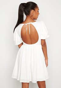 Bíl dress s designem nabíraných rukávů, otevřeným zadním dílem zabezpečeným tkaničkou a rozšířenou sukní, která končí nad koleny. Měkká, lehká tkanina.