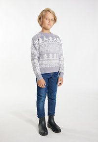 Grijze gebreide trui met witte winterpatronen, blauwe spijkerbroek en zwarte rubberen laarzen. Kind staat in een neutrale pose tegen een lichte achtergrond.