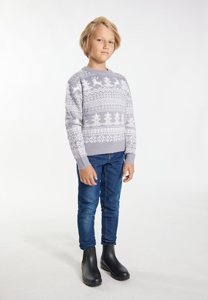 Grijze gebreide trui met witte winterpatronen, blauwe spijkerbroek en zwarte rubberen laarzen. Kind staat in een neutrale pose tegen een lichte achtergrond.