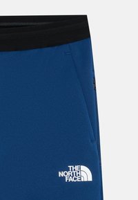 Mėlynos sportinės kelnės su juodu juosmeniu, puošiančiu baltu logotipu. Pagamintos iš sklandžios, tamprios medžiagos; turi užtrauktukais uždaromas šonines kišenes.