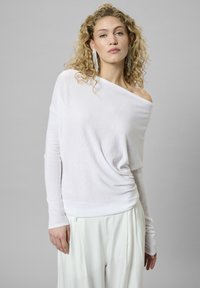 Fehér, váll nélküli, hosszú ujjú blúz, drap�ált dizájnnal, puha textúrával és karcsúsított derékkal, fehér, bő szárú nadrággal párosítva.