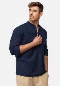 Mörkblå långärmad skjorta med en knäppt henley-krage och mjukt material. Har en avslappnad passform och diskret sömnad i sidorna.