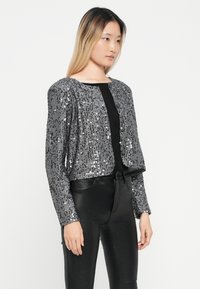 Korte sequins jas in zilver en zwart, voorzien van een ronde kraag en knoopsluiting, met glanzende sequins op een zachte stof.