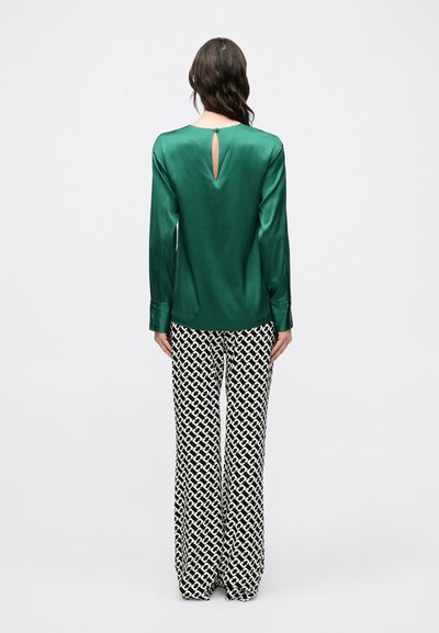 Πράσινη σατέν μπλούζα με μακριά μανίκια και λεπτομέρεια με άνοιγμα στην πλάτη, συνδυασμένη με μαύρο-άσπρο παντελόνι φαρδιάς γραμμής με σχέδια. Λείο ύφασμα, άνετη εφαρμογή.