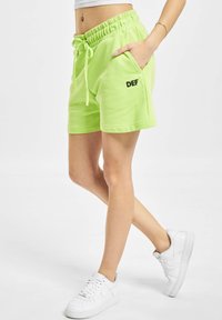 Neongrüne Baumwollshorts mit elastischem Bund und Kordelzug, ausgestattet mit Seitentaschen und dem aufgedruckten Text "DEF" in Schwarz.