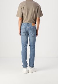 Dopasowane jasnoniebieskie dżinsy z tylnymi kieszeniami i brązową skórzaną naszywką. Połączone z gładkim beżowym t-shirtem i białymi tenisówkami.