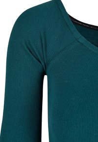 Tyrkysová ribbovaná tkanina má přiléhavý střih s širokým výstřihem a hladkou strukturou. Viditelné švy zvýrazňují konstrukci.