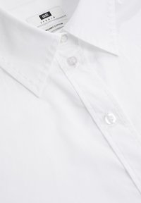 Camicia bianca con bottoni realizzata in cotone biologico. Presenta un colletto classico, apertura con bottoni e dettagli di cucitura sottili lungo i bordi.