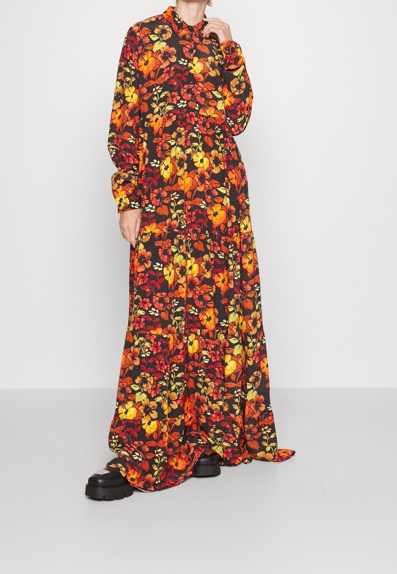 Lange, bloemenjurk met een zwarte achtergrond, met levendige oranje, rode en gele bloemen. Lange mouwen en een kraag, vloeiende zoom.
