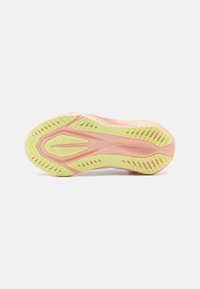 Chaussure de course avec une tige rose, semelle extérieure texturée jaune avec des rainures à motifs, et un design épuré pour traction et soutien.