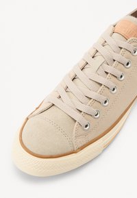 Baskets en toile beige avec un bout en suède texturé, un design classique à lacets et une semelle en caoutchouc dotée d'une grippe à motif.