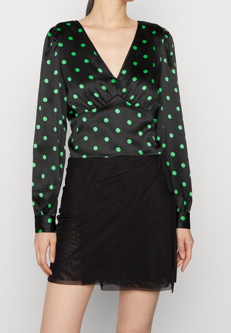 Top in satin nero con pois verdi, scollatura a V profonda, busto arricciato e maniche lunghe. Abbinato a una gonna lunga trasparente nera.