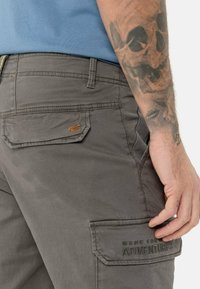 Grå cargo shorts med flere lommer, en tekstureret stofkvalitet og syninger som accent. "Made for Adventures" er broderet på baglommen.