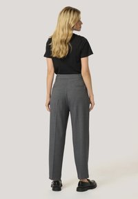 Gray high-waisted trousers with a tailored design, featuring pleats, a back pocket, and a smooth texture, paired with a black t-shirt.