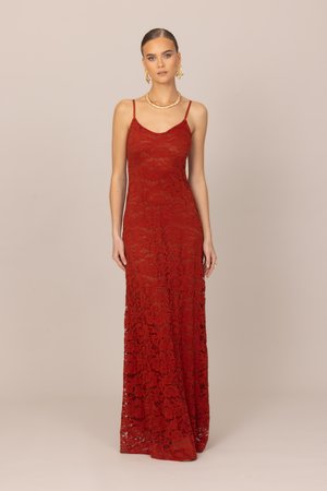 Femme aux cheveux tirés en arrière portant des boucles d'oreilles et un collier en or, vêtue d'une robe rouge en dentelle longue jusqu'au sol avec des bretelles fines.