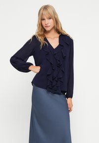 Blusa navy con frontale arricciato, scollo a V e maniche lunghe; abbinata a una gonna in satin azzurro chiaro e liscia. Texture del tessuto morbida.