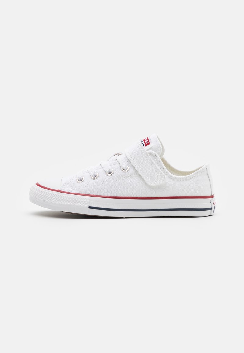 Witte canvas sneakers met een ronde neus, veters en klittenbandsluiting, rode en blauwe accenten op de zool, en een gestructureerde rubberen buitenzool.