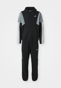 Black and gray Nike tracksuit with hoodie and jogger pants, featuring white Nike logos on chest and thigh, elastic cuffs on sleeves and ankles.