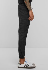 Fekete tapered joggerek texturált anyagból, gumis derekúval és oldzsebekkel. Fehér tornacipővel párosítva, fekete csíkokkal.