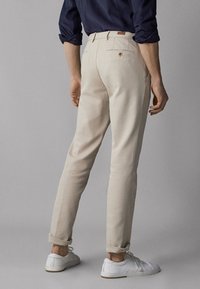 Beiga byxor med slim fit och uppvikta fållar. Tillverkade av ett mjukt material och har en bakficka med en knappdetalj. Bärs med vita sneakers.