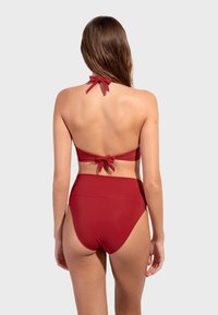 Crveni dvodijelni bikini s halter dekolteom i trakama na vezanje te visokim donjim dijelom. Glatka tekstura i jednolična boja.