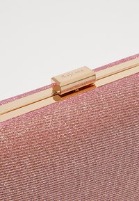 Gros plan d'une pochette rose pailletée avec un fermoir métallique doré gravé du mot « MASCARA ».