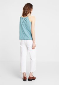 Un haut bleu clair sans manches avec un col froncé, associé à un pantalon blanc raccourci avec des ourlets effilochés et des chaussures marron.