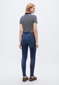 Sötétkék slim-fit farmernadrágot párosítanak egy tengerészkék-fehér csíkos, rövid felsővel, amely klasszikus szabású és minimalista kialakítású.