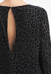 Svart leopardmönstrad klänning med hög krage, öppen rygg och textil med sammetsliknande accenter. Guldknappstängning vid halsen.