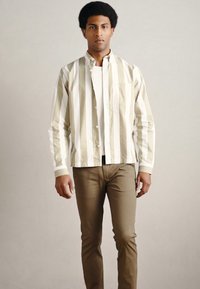 Lichtgewicht gestreept overhemd in beige en wit, met knoopsluiting aan de voorkant. Gecombineerd met strakke bruine broek. Soepele textuur en casual stijl.