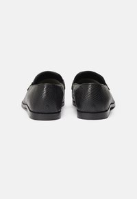 Black slip-on shoes with a textured leather exterior, low-profile design, rounded toe, and a flat rubber sole. No notable embellishments.