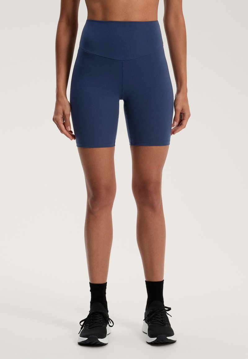 Magasan szabott, sötétkék, elasztikus anyagból készült rövidnadrág, sima textúrával, testhezálló fazonnal és a comb közepéig ér.