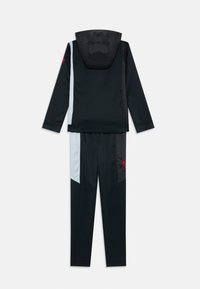 Ensemble de survêtement noir en deux pièces avec veste à capuche et pantalon, comportant des panneaux latéraux argentés et un petit logo circulaire rouge sur le bras et la jambe.