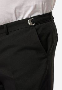 Pantaloni neri realizzati in tessuto liscio, caratterizzati da una fibbia argentata, tasche laterali e una vestibilità sartoriale. Scatto in primo piano che mette in evidenza i dettagli.