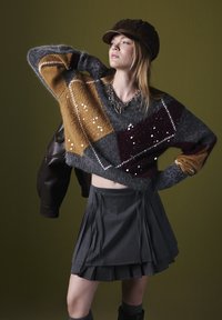 Grau gestrickter, kurzer Pullover mit mehrfarbigem Rautenmuster und Pailletten, kombiniert mit einem grauen Faltenrock und einer braunen Mütze.