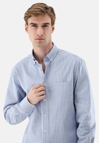 Hellblau-weiß gestreiftes Hemd mit Knöpfen, Kragen, langen Ärmeln und Brusttasche. Der Stoff wirkt glatt und hat eine weiche Textur.