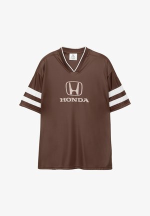 Smeđi sportski dres s V-izrezom, bijele horizontalne pruge na rukavima i s logotipom Honde istaknutim na prednjoj strani.